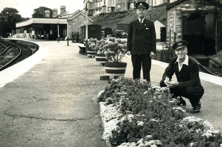 Two members of Staff on the platform at Kingsbridge Station. Tubs of flowers along the platform. 1960