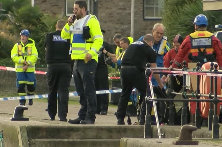 A rescue responder talks into a handset radio as police and coastguard crew prepare on the edge of the River Dart
