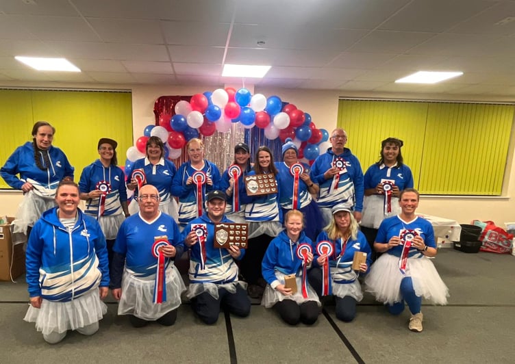 Two Bridges Flyball teams, with their awards from Indoor National Flyball Championships 2025 and wearing tutus in memory of team member Jo Paton.