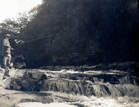 Sidney Dent fishing from  bank of river by small rapids
